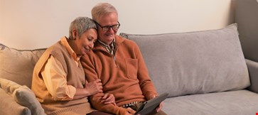 Happy senior old couple sit on sofa using digital tablet