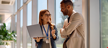 Happy business colleagues communicating while using laptop