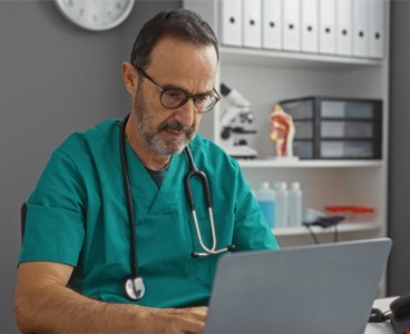 Hispanic man in hospital clinic room wearing medical scrubs and glasses
