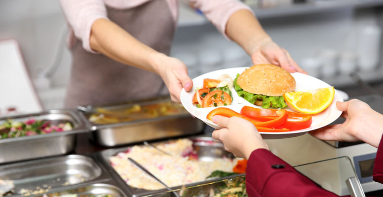 Pleasant woman giving lunch to school girl in cafeteria