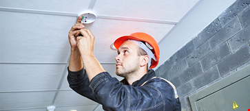 Worker installing smoke detector on ceiling