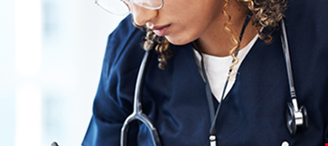 Focused healthcare professional taking notes while working on a laptop