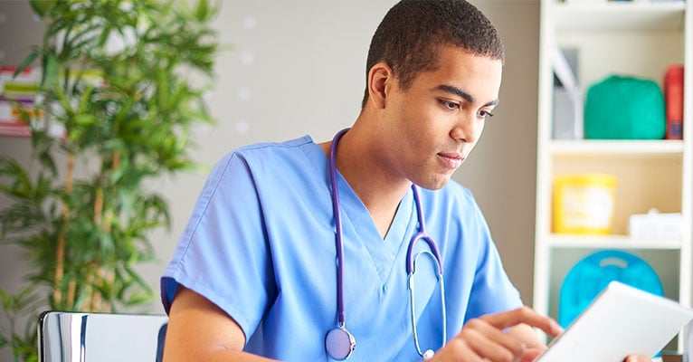 Female doctor wearing scrubs in hospital corridor using digital tablet